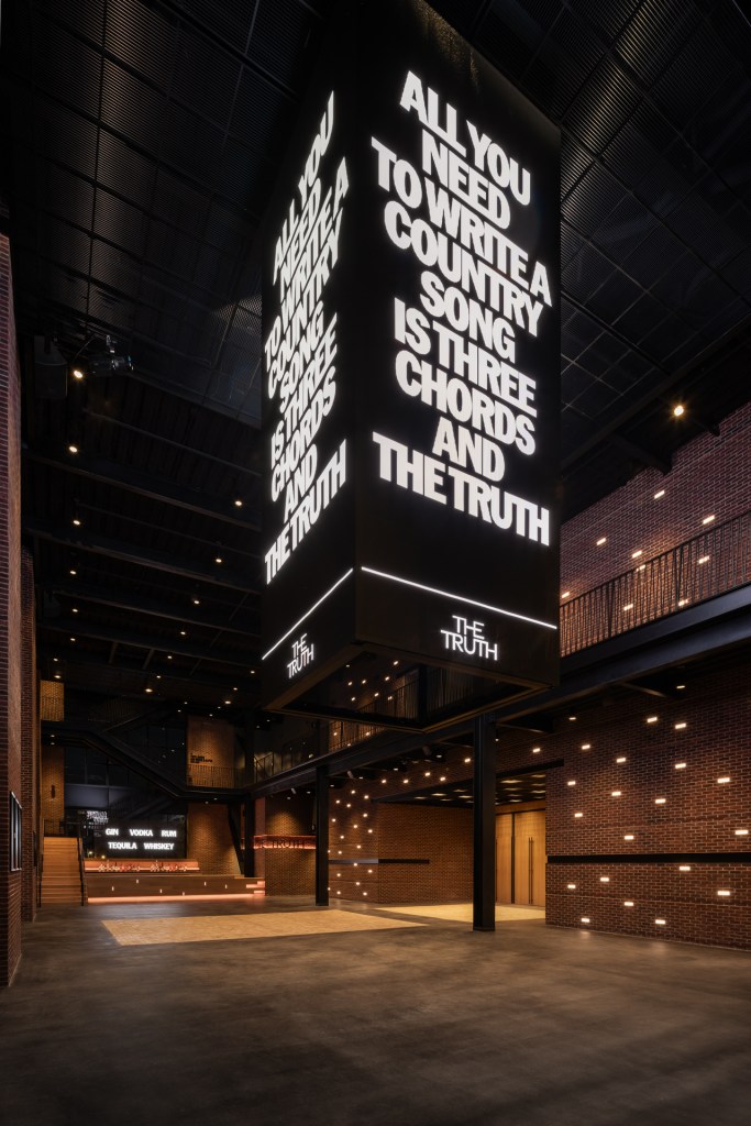 An interior space inside The Truth with a large vertical, multi-sided sign that says "All you need to write a country song is three chords and the truth."