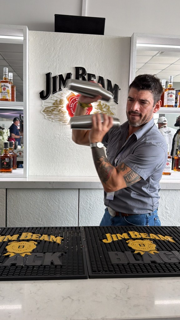 A bartender with two cocktail shakers standing in front of a white Jim Beam sign.