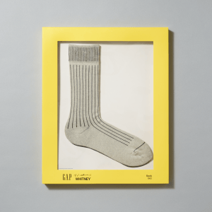 A pair of heather gray crew socks inspired by Roy Liechtenstein's Sock (1962) painting in their yellow packaging