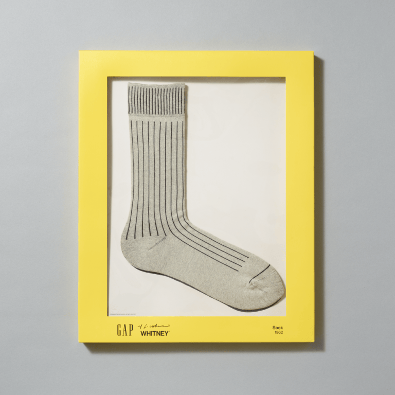 A pair of heather gray crew socks inspired by Roy Liechtenstein's Sock (1962) painting in their yellow packaging