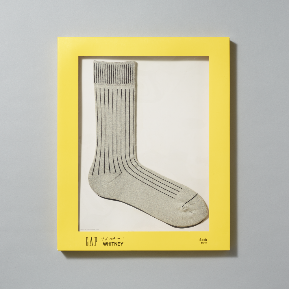 A pair of heather gray crew socks inspired by Roy Liechtenstein's Sock (1962) painting in their yellow packaging